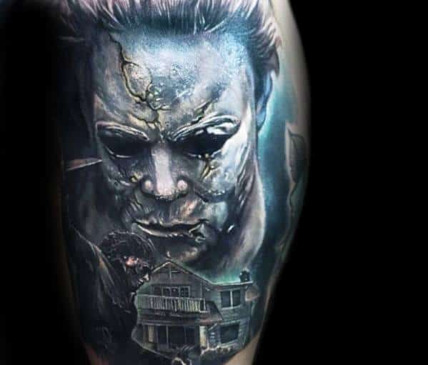 Realistic Michael Myers tattoo with a cracked mask, eerie blue tones, and the infamous house below for a chilling horror design.