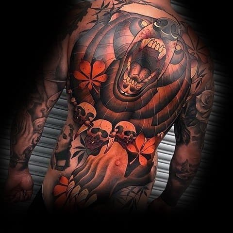 Neo-traditional full-back bear tattoo featuring a roaring bear with bold black and orange shading, skulls, floral elements, and tribal influences.