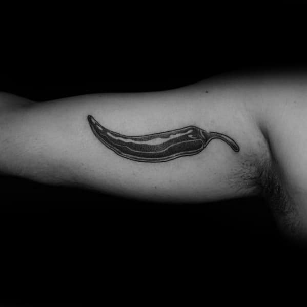 Black and grey chili pepper tattoo on the inner arm with smooth shading and fine details, creating a sleek and realistic design.