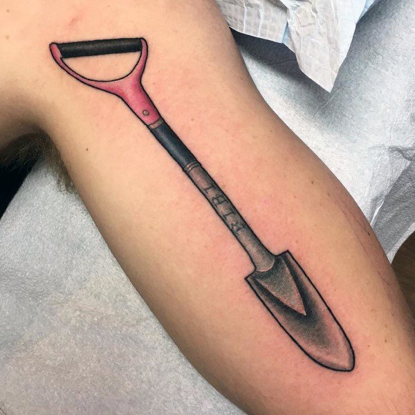 Realistic shovel tattoo with a red and black handle and shaded metal blade, placed on the arm, symbolizing labor, resilience, and perseverance.