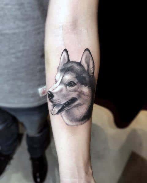Realistic Siberian Husky tattoo on a man's forearm, showcasing fine shading, lifelike fur texture, and a happy expression.