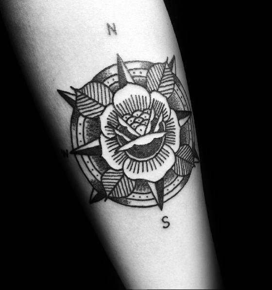 Tattoo of a compass rose with a detailed rose design at the center on forearm, labeled with cardinal directions.