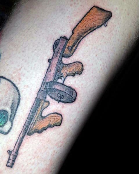 Detailed Tommy gun tattoo with a classic wood grain effect on the stock and grip, featuring bold black outlines and shading for a vintage firearm look.