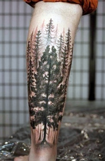 Realistic forest tattoo on the leg, featuring detailed pine trees with subtle shading and a misty background for a deep, nature-inspired design.