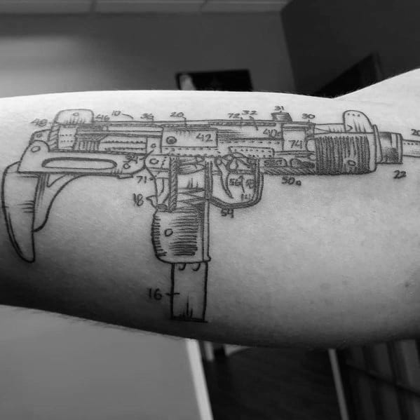 Technical blueprint-style Uzi tattoo on the forearm, featuring intricate mechanical details and numbered annotations for a schematic effect.