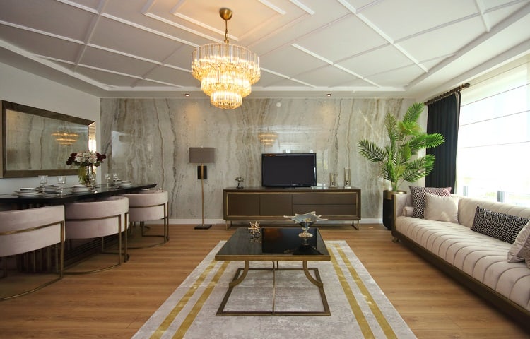 A stylish modern living room featuring a textured ceiling, luxurious furniture, a chandelier, and a marble accent wall, creating an elegant and inviting space