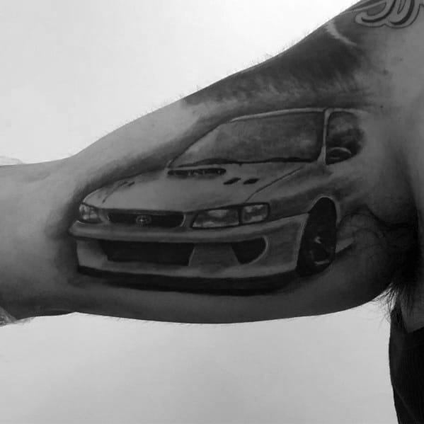 Realistic black and grey Subaru Impreza tattoo on the inner arm, featuring a detailed front view of the iconic rally-inspired performance car.