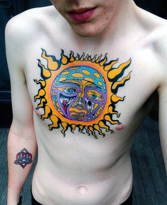 Bright and bold Sublime sun face tattoo centered on the chest, with vibrant yellow flames, blue and purple tones, and vivid expression.
