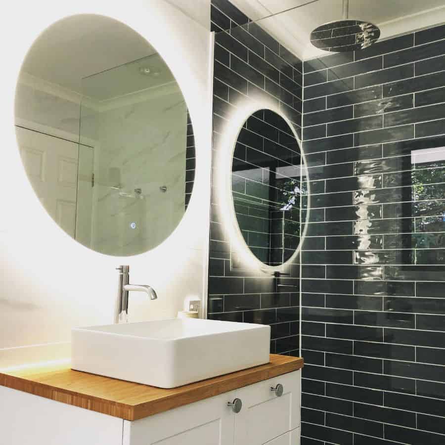 Modern bathroom with backlit round mirror, green subway tile shower, and vessel sink.