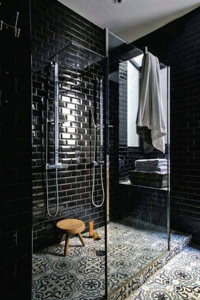 Black subway tile shower with glass enclosure, patterned floor tiles, and wooden stool.