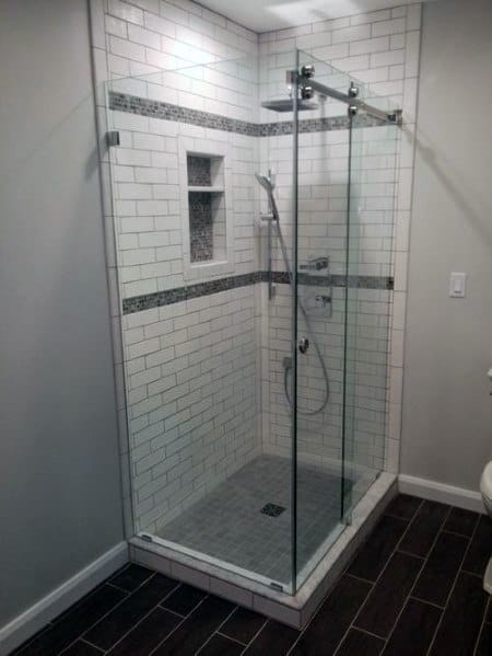 Modern corner glass shower with white subway tiles, a built-in shelf, and gray tile floor
