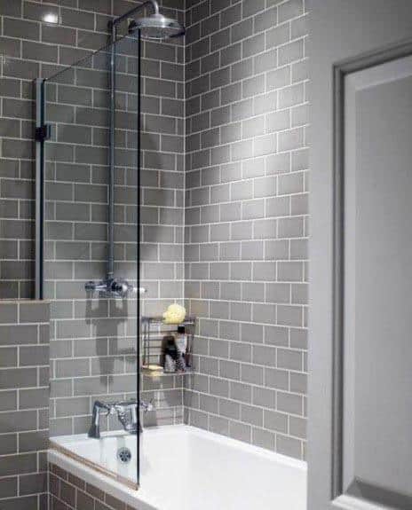 A gray bathroom featuring subway tiles, a sleek glass shower divider, and a compact tub for a clean and modern look.
