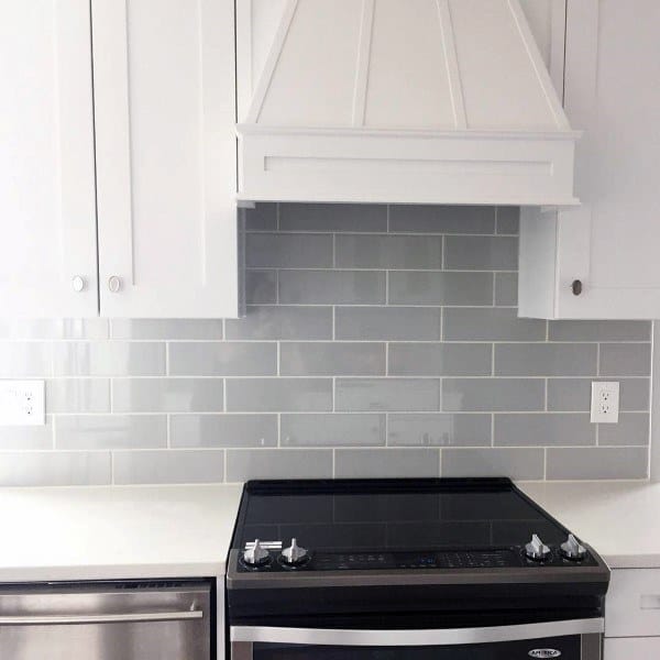 White kitchen cabinets with a gray subway tile backsplash and black electric stove.
