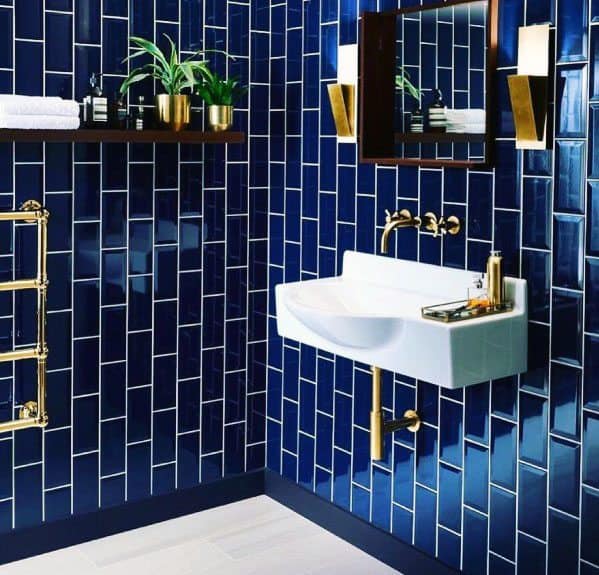Bathroom with glossy navy subway tiles, white grout, gold fixtures, and floating shelf.