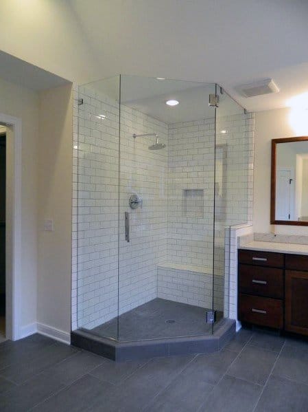 Modern bathroom featuring a corner shower with glass enclosure, white subway tiles, and a wooden vanity with mirror