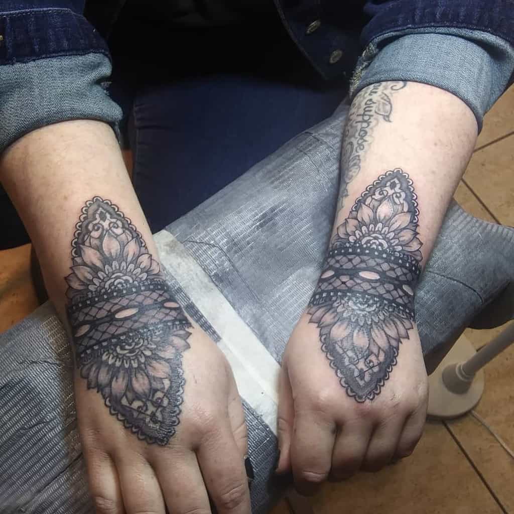 Symmetrical black lace tattoos on both hands, featuring intricate mandala and floral patterns with bold shading and ornamental details.