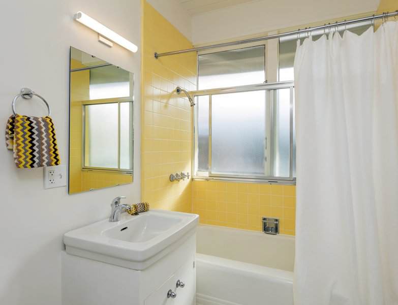 White bathroom with bright yellow wall tiles around the bathtub, a matching patterned towel, and a simple vanity.