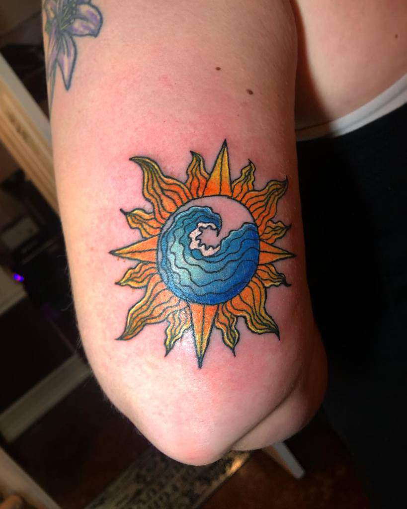 Colorful tattoo featuring a stylized sun with an ocean wave at its center, blending fire and water elements