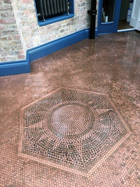 Penny floor with a sunburst pattern surrounded by a hexagonal border near a brick wall.