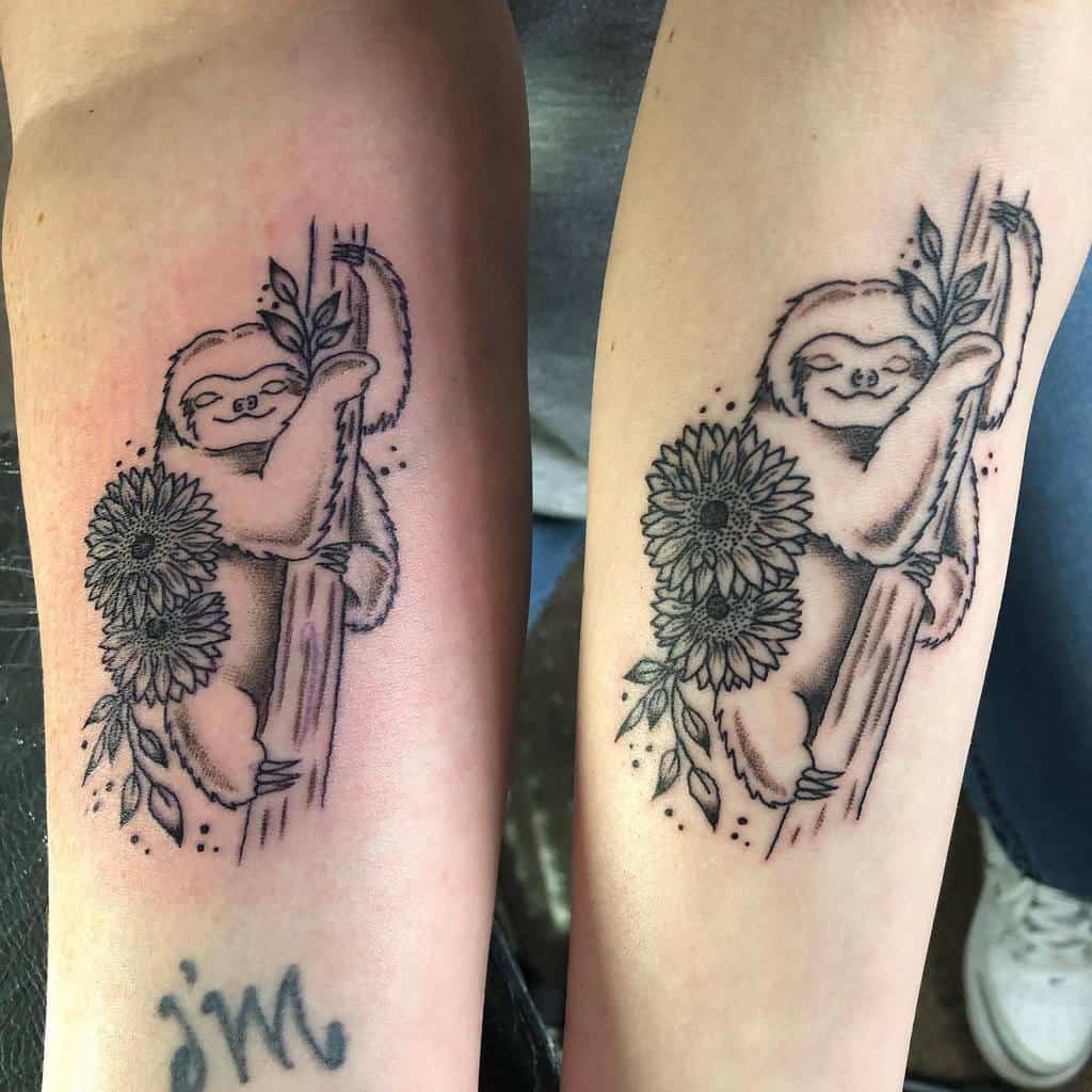 Matching mother-daughter tattoos of a sloth hugging a branch adorned with sunflowers and leaves, in black ink