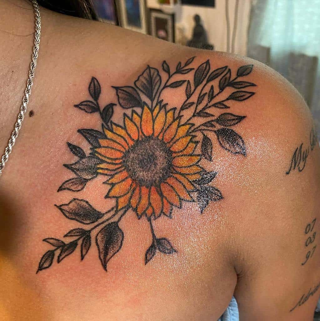 A vibrant sunflower and leaves tattoo on a shoulder