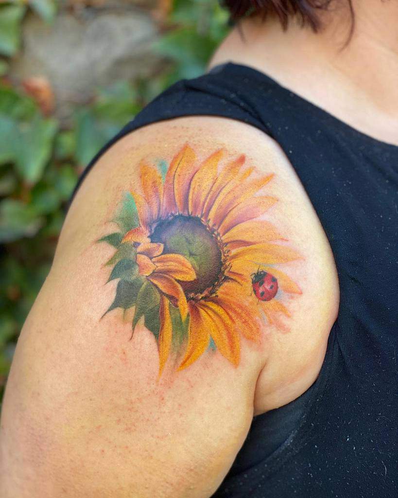 A vibrant sunflower tattoo, complete with a small red ladybug, adorns a person's shoulder