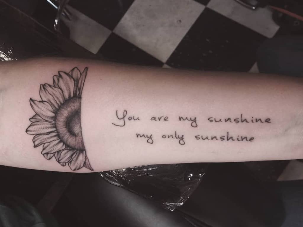 Tattoo of a sunflower and the phrase "You are my sunshine, my only sunshine" on an arm