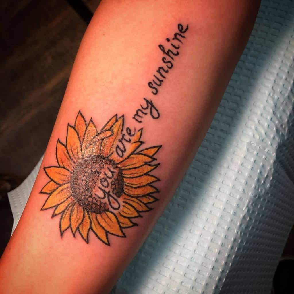 Tattoo of a sunflower with "you are my sunshine" text on a person's arm