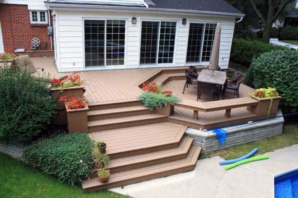 Wooden patio deck with table, chairs, bench, and potted plants leading to a brick house with sliding glass doors