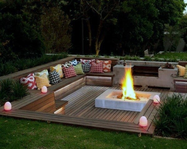 Sunken fire pit with cozy wooden seating and colorful cushions.