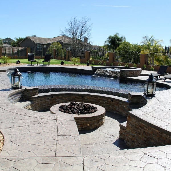 Sunken fire pit with stamped concrete flooring, set beside a serene pool and waterfall.