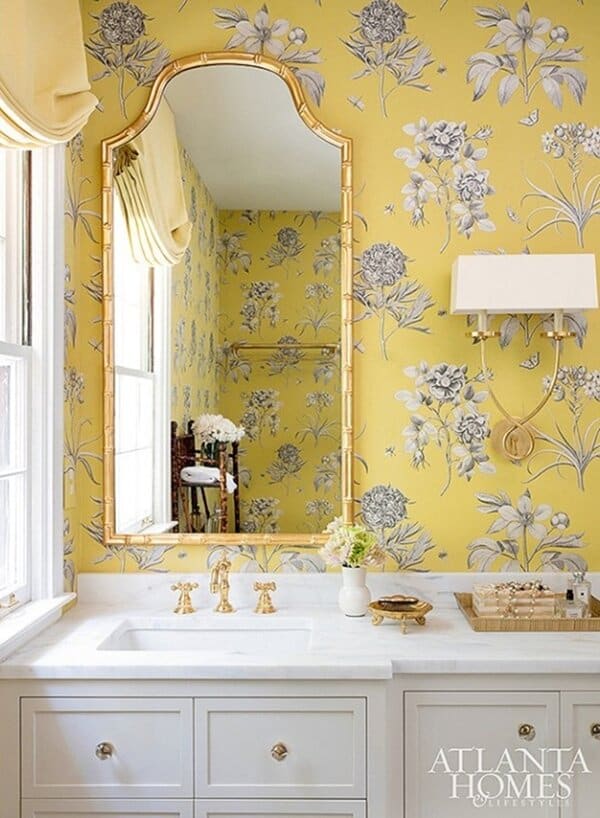 Powder room featuring yellow floral wallpaper, a decorative framed mirror, marble vanity, and gold fixtures for a bright, elegant look.