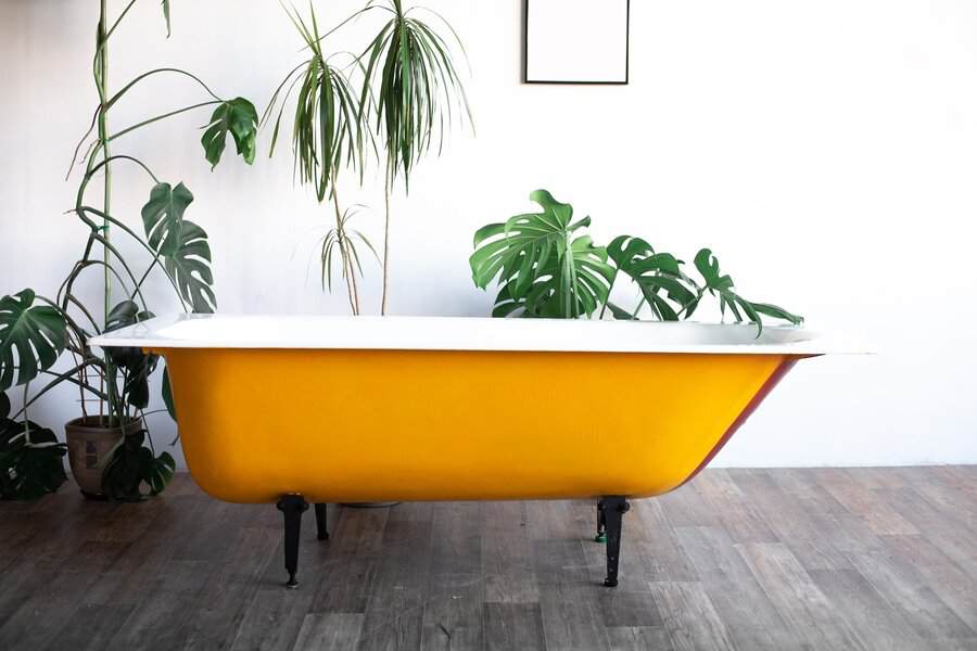Bold yellow clawfoot bathtub surrounded by lush green plants for a lively bathroom look.