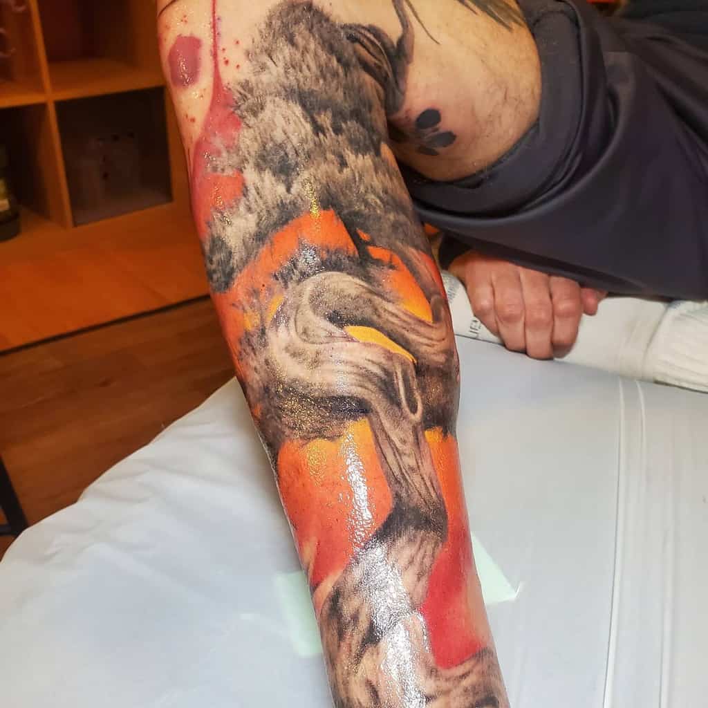 A detailed, colorful leg sleeve tattoo featuring abstract large tree with yellow, orange and red background