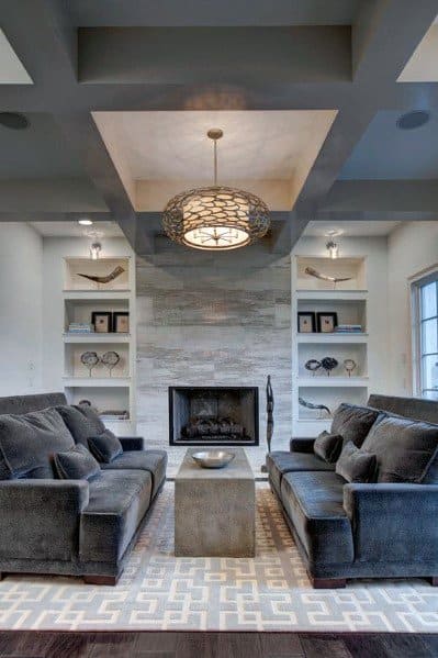 Modern living room with a central fireplace framed by built-in bookcases, flanked by two plush grey sofas, geometric area rug, and a statement ceiling light.
