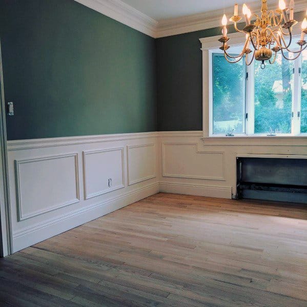 Empty room with green walls, chair rail wainscoting, a large window, wooden floor, and a chandelier