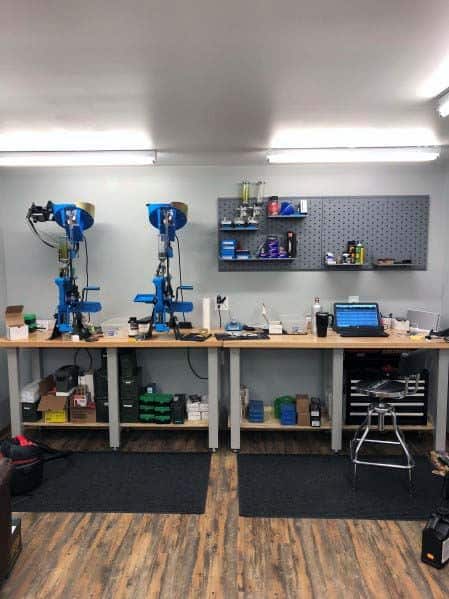 Modern and spacious reloading bench featuring dual reloading presses, ample counter space, and clean organization. The layout incorporates well-lit surroundings, pegboard wall storage, and sturdy shelving for an efficient and tidy workspace.