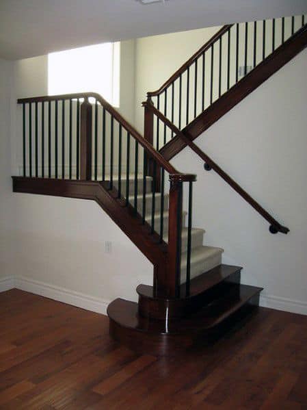 Dark wood staircase with black metal balusters and wall-mounted handrail in a spacious room.