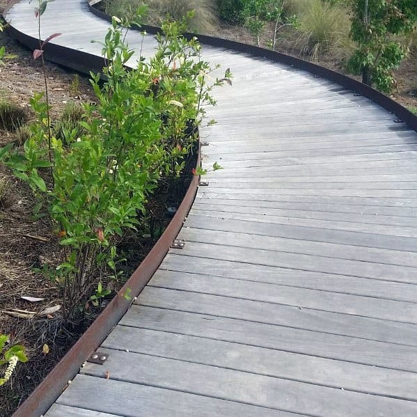 Curved wooden walkway surrounded by greenery and plants