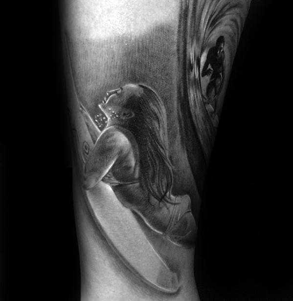 Black and grey tattoo of a woman paddling on a surfboard with a surfer riding a wave in the background, capturing ocean life and movement.