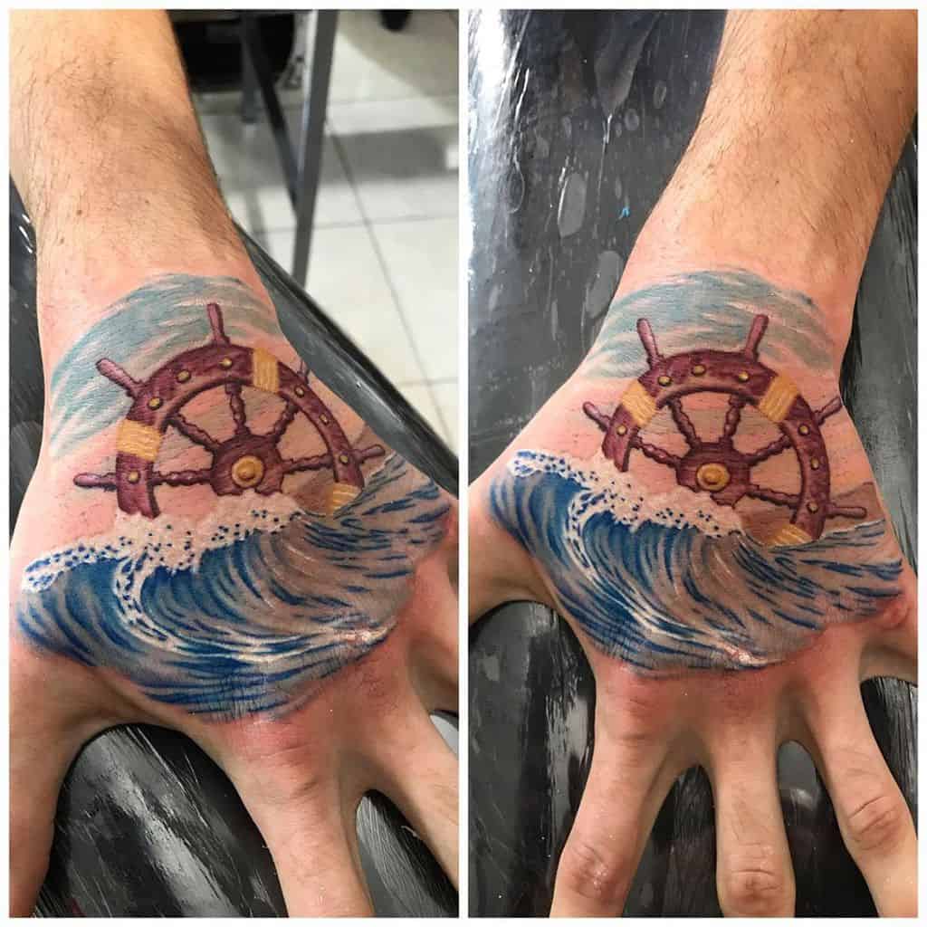 Colorful tattoo featuring a wooden ship's wheel partially submerged in ocean waves, with blue and white water details