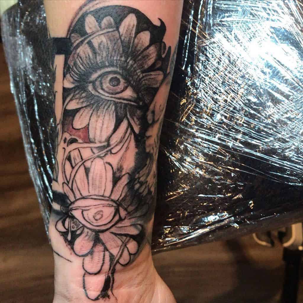 Forearm tattoo black and grey shading surreal daisies with eyes