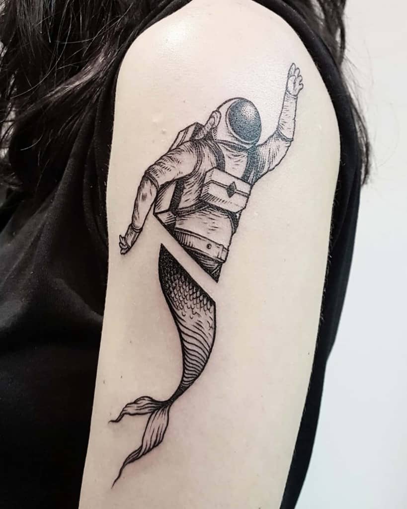 Black and grey tattoo of a surreal astronaut-mermaid hybrid, with the body split between a space suit and a mermaid tail, floating in motion.
