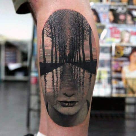 Surreal tattoo of a forest path merging with a woman's face and water reflection, creating a dreamy double exposure effect.