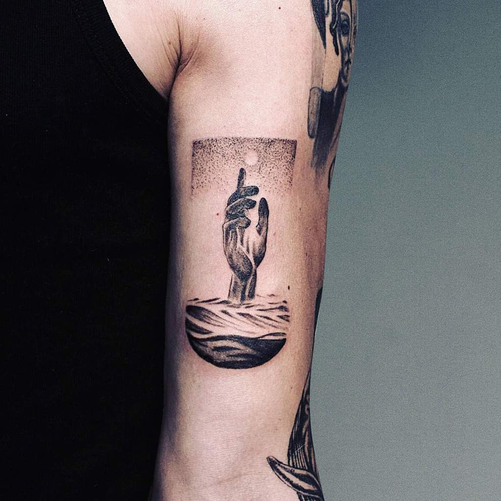 Surreal tattoo featuring a realistic hand emerging from ocean waves, reaching towards the moon in a dotwork sky