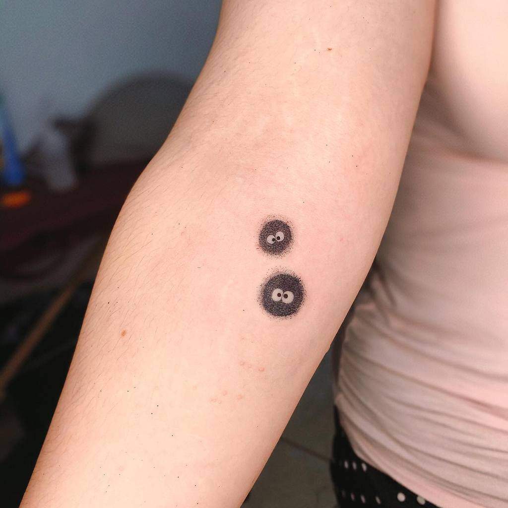 Minimalist Totoro-inspired soot sprites tattoo, featuring two cute, tiny sprites on the forearm, capturing a playful Ghibli essence