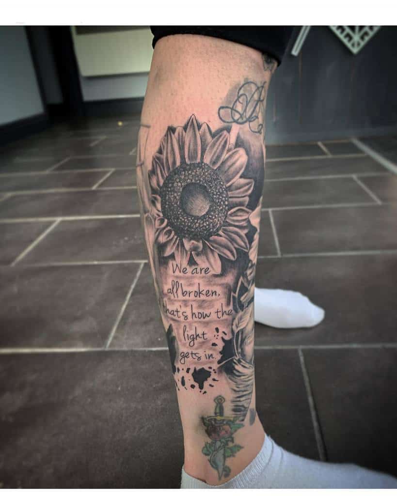 Tattooed leg sleeve with a large sunflower, quote "We are all broken, that's how the light gets in," with sword and rose wrapping it