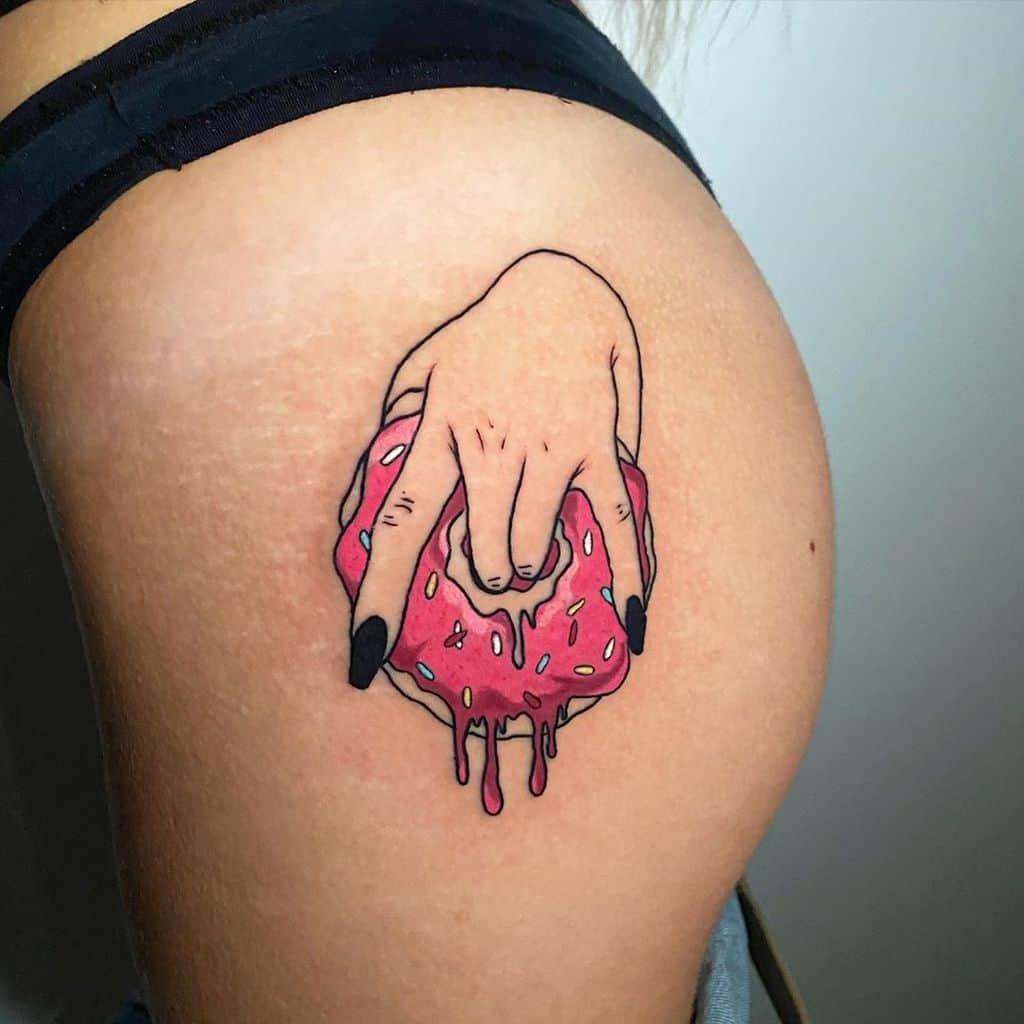 A colorful tattoo of a hand with black nails squeezing a dripping pink-frosted donut, placed on the hip in a bold and provocative style.