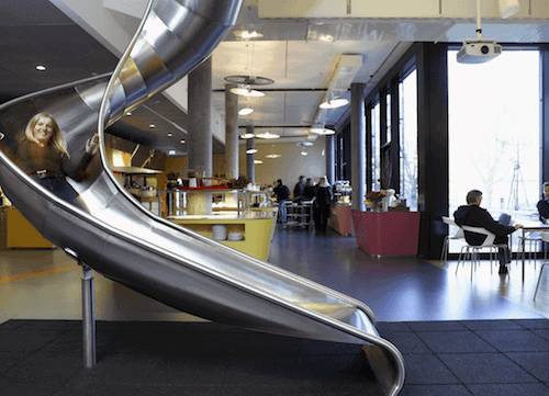 Woman joyfully sliding indoors at a modern café, with chatter and coffee aroma filling the background