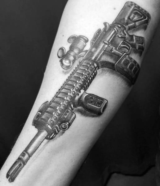 Highly detailed black and grey AR-15 tattoo on the forearm, featuring a tactical scope, grip, and rail system, symbolizing precision and strength.